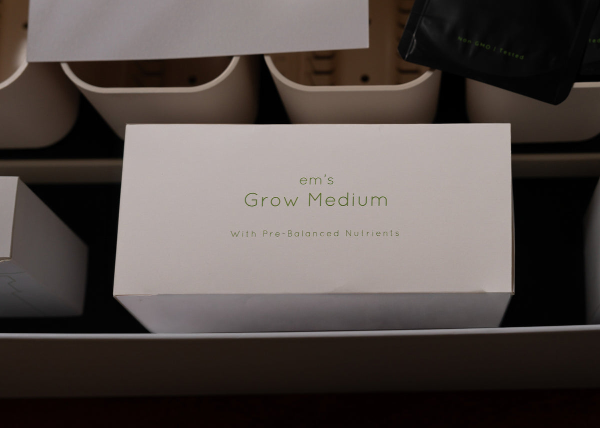 A white rectangular box labeled 'em's Grow Medium With Pre-Balanced Nutrients' in green text, placed inside a tray with other containers around it.