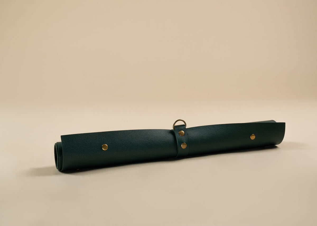 50x75cm in size, A rolled dark green leather portfolio or organizer case with brass grommets and a metal ring, shown on a neutral beige background.