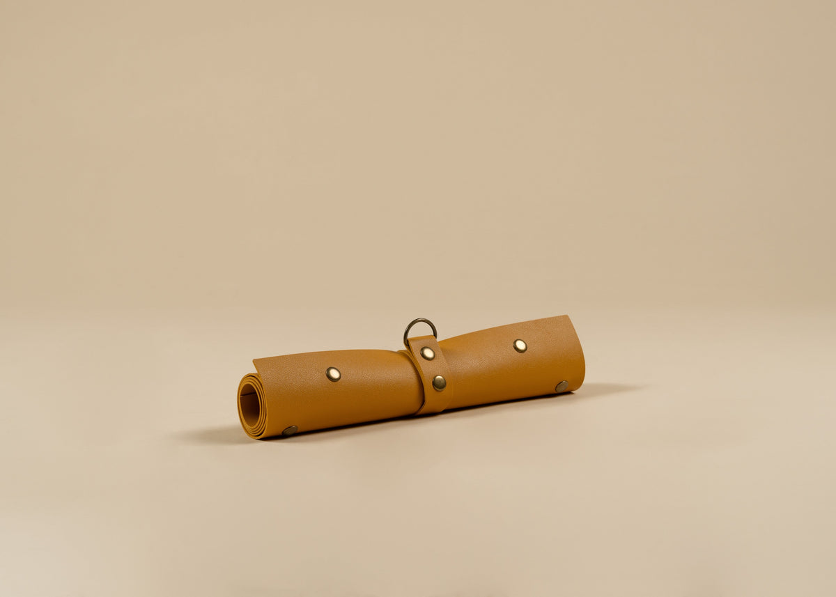 30x60cm in size, A rolled yellow leather pouch or case with metal rivets and a small ring detail, photographed on a plain warm beige studio background.