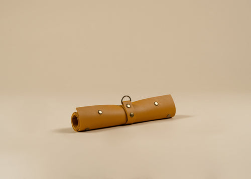 30x60cm in size, A rolled yellow leather pouch or case with metal rivets and a small ring detail, photographed on a plain warm beige studio background.