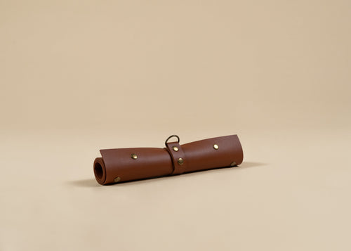 30x60cm in size, A rolled brown leather portfolio or organizer sleeve with brass grommets and a metal loop, resting on a solid beige background.