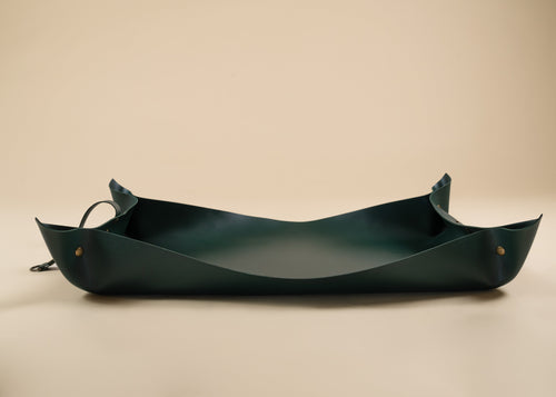 50x75cm in size, A dark green leather tray with a curved, boat-like shape and small brass grommets, shown on a plain beige background.