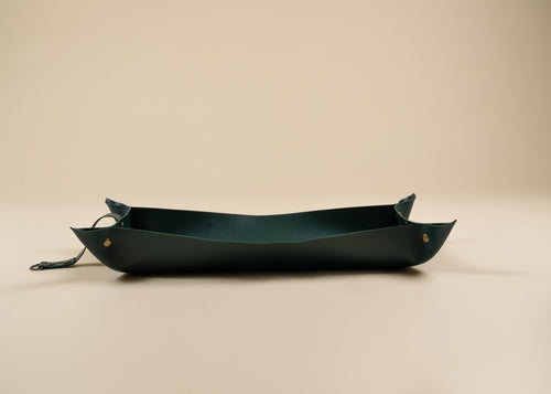 30x60cm in size, A dark forest green leather boat-shaped tray with brass rivets and a matching leather strap, photographed on a solid beige background.