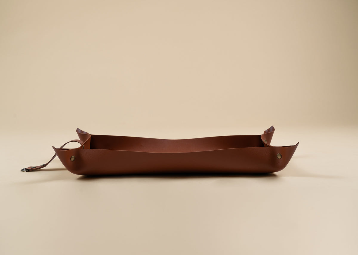 30x60cm in size, A brown leather tray with a long strap and small metal rivets, photographed on a plain beige studio background.
