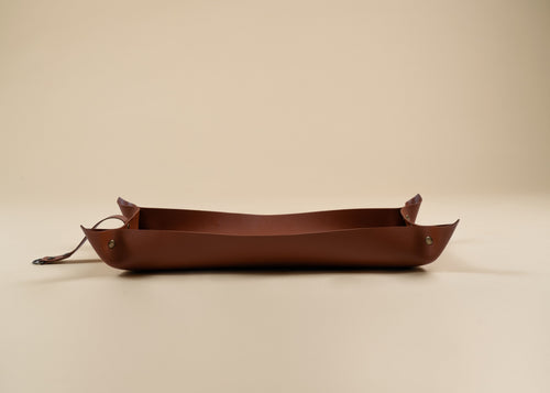 30x60cm in size, A brown leather tray with a long strap and small metal rivets, photographed on a plain beige studio background.