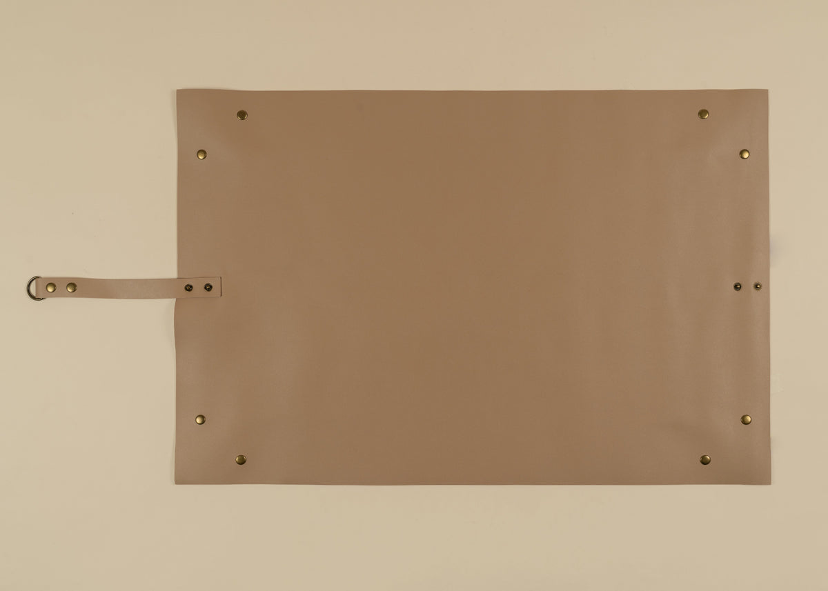 50x75cm in size, A rectangular tan leather or faux-leather pad with brass grommets and a matching strap on the left side, photographed flat against a light beige background.