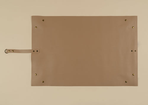 50x75cm in size, A rectangular tan leather or faux-leather pad with brass grommets and a matching strap on the left side, photographed flat against a light beige background.