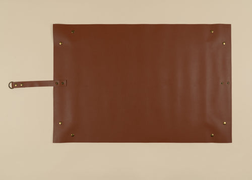 50x75cm in size, A brown leather roll-top pouch or sleeve with brass grommets and a strap on the left side, laid flat on a light beige background.