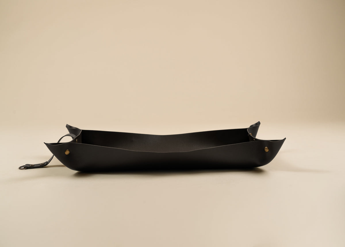 30x60cm in size, A black leather boat-shaped tray with small brass rivets and a hanging loop, photographed on a plain beige background.