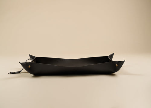 30x60cm in size, A black leather boat-shaped tray with small brass rivets and a hanging loop, photographed on a plain beige background.
