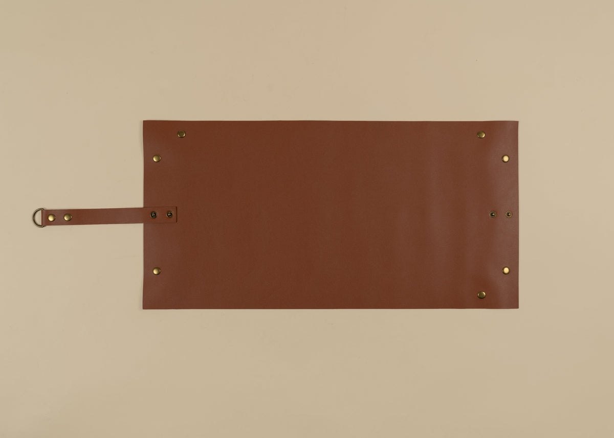30x60cm in size, A brown leather apron or roll-up pouch with brass grommets and a strap, laid flat on a beige background.