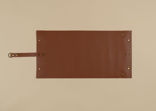 30x60cm in size, A brown leather apron or roll-up pouch with brass grommets and a strap, laid flat on a beige background.