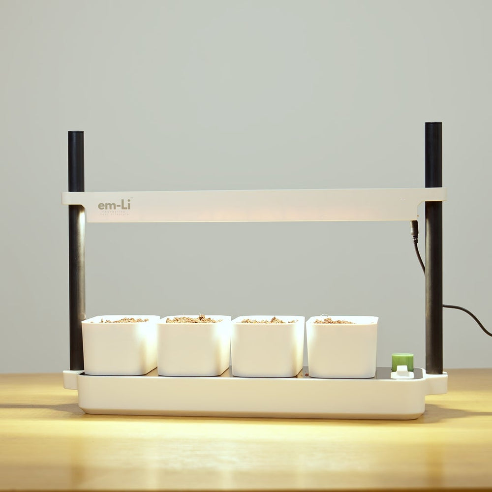 An em-li indoor smart garden light with four white pots on a wooden table against a neutral gray wall.