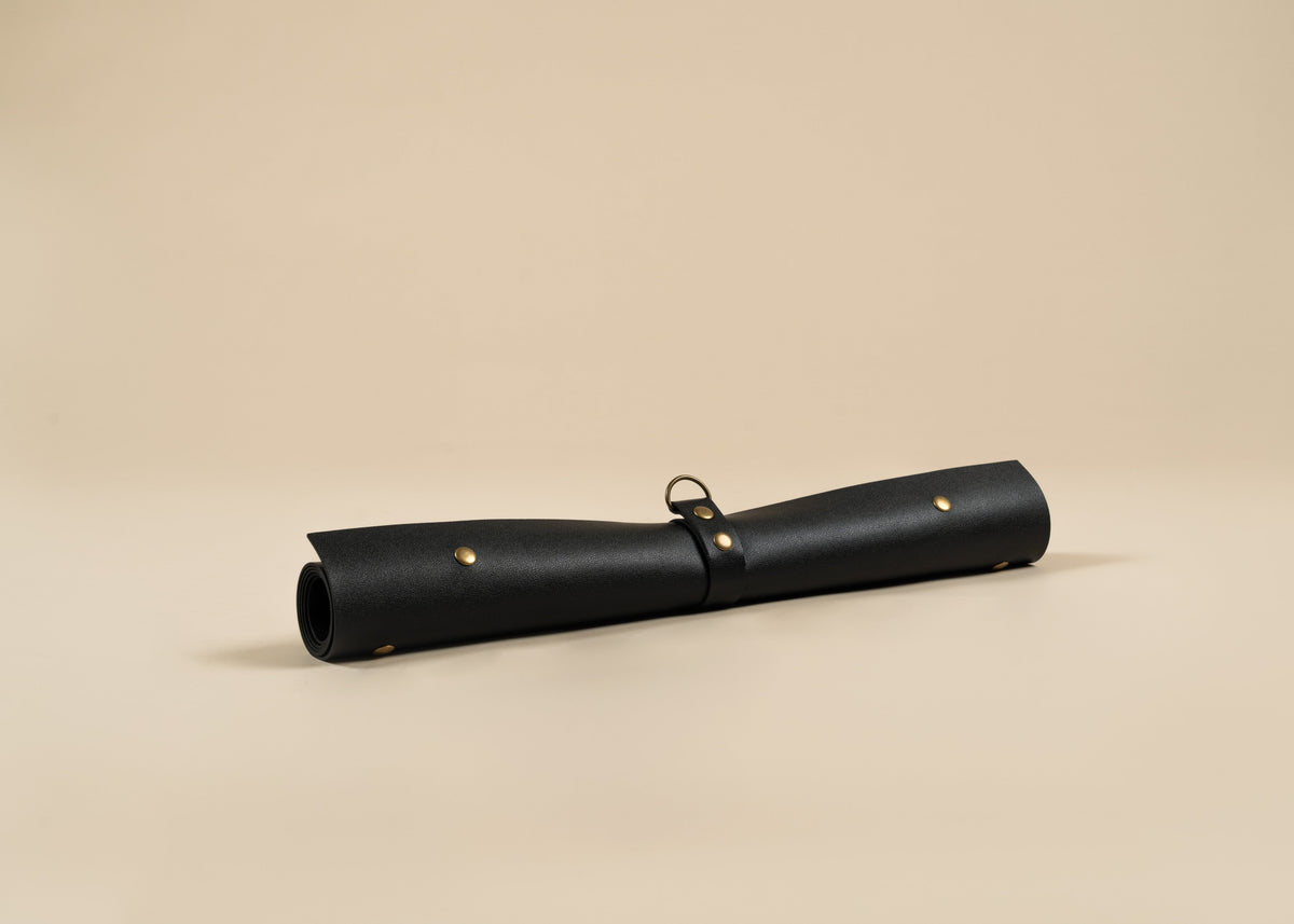 50x75cm in size, A black rolled leather sleeve or scroll holder with brass grommets and a black strap, photographed on a plain beige studio background.