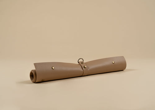50x75cm in size, A rolled beige leather sleeve or pouch with brass-tone rivets and a small metal ring, photographed on a plain warm beige studio background.