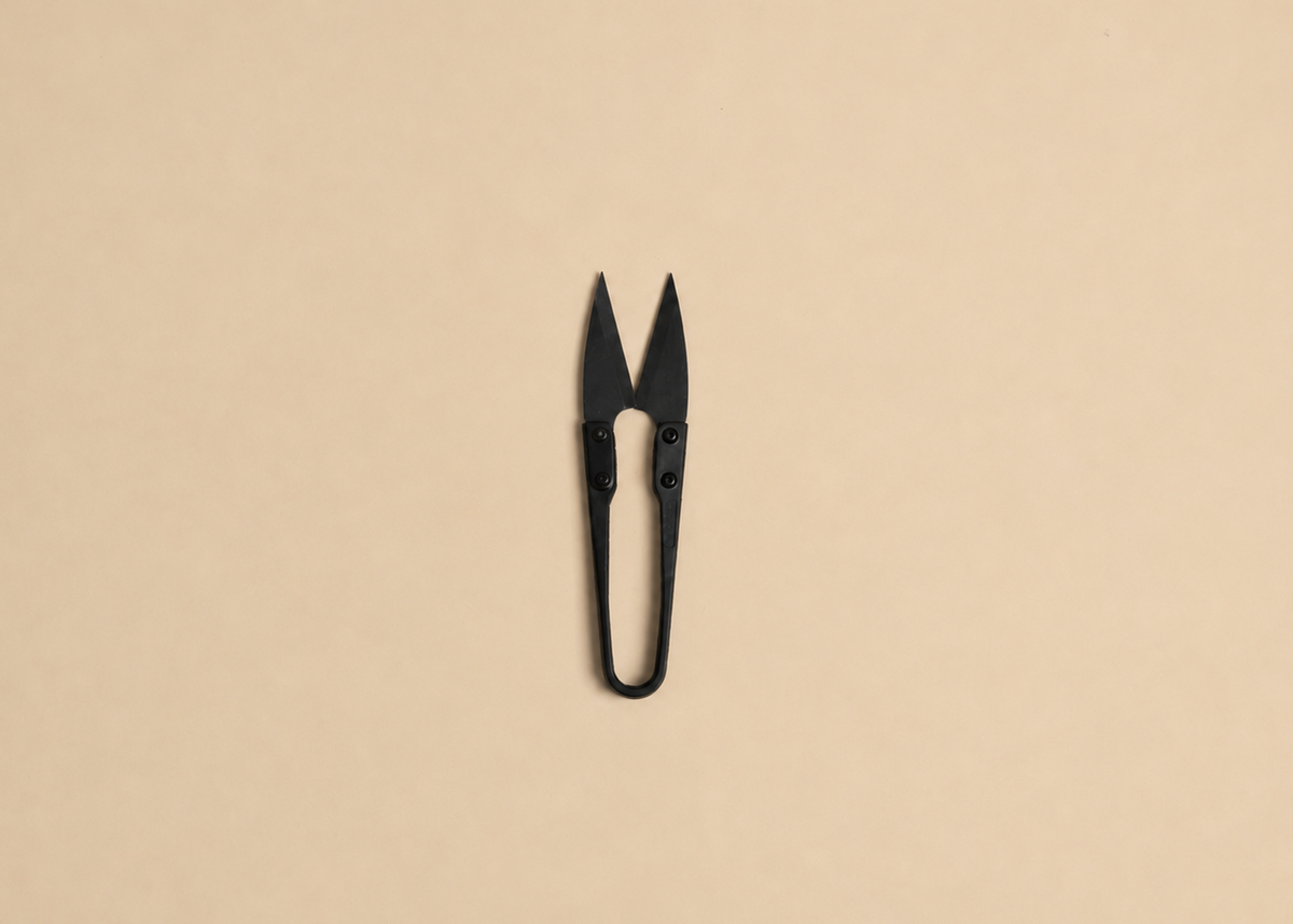 A pair of small black scissors or nail nippers centered on a plain warm beige background.