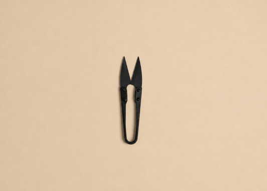 A pair of small black scissors or nail nippers centered on a plain warm beige background.